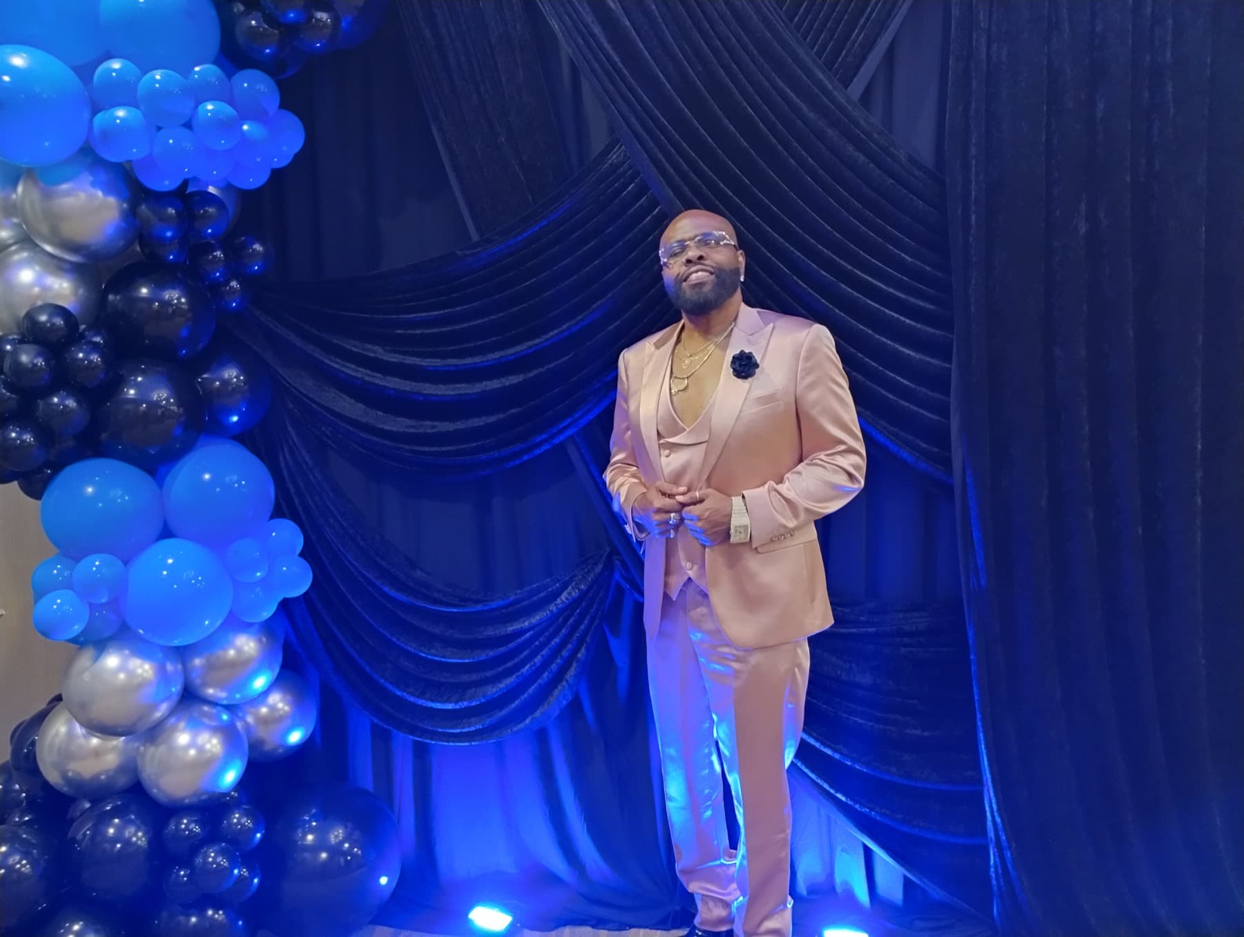 Dr. Fain dressed for an event in front of blue and black stage decor with balloons